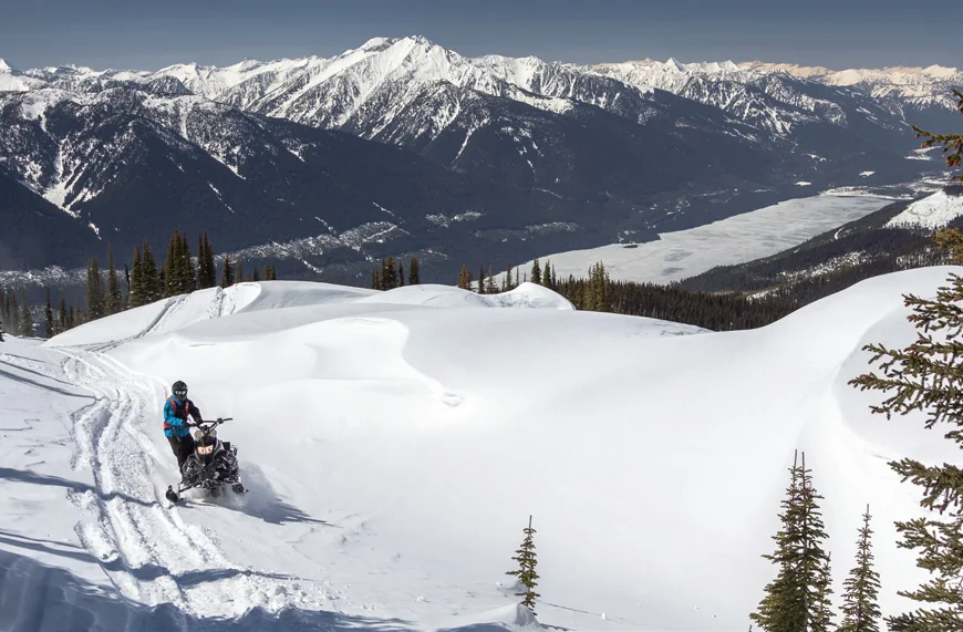 Snowmobiler in the Foggy Day riding area below a corniced ridge
